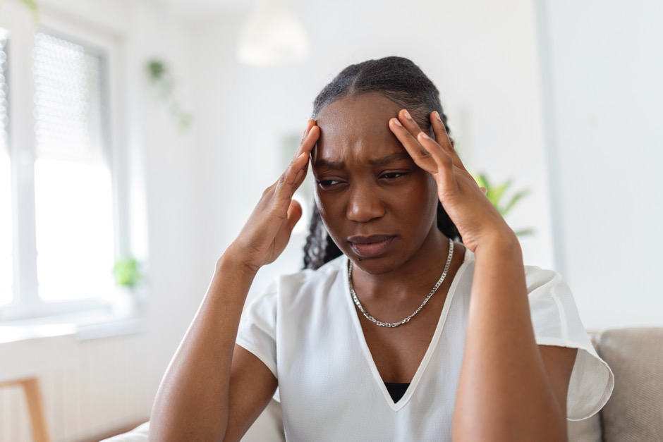 A woman in a white dress holds her hands to her head as though she has a headache.