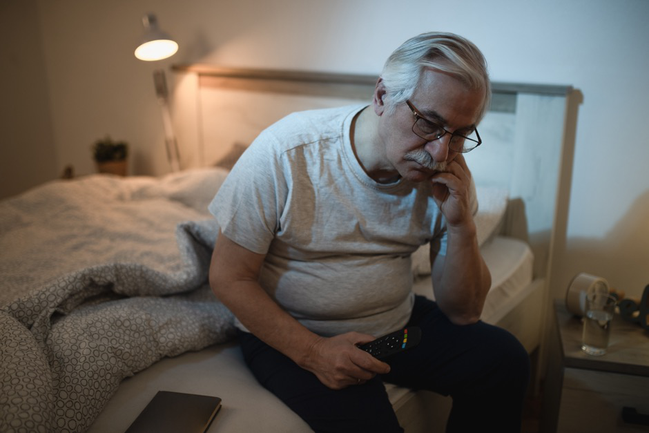 A man sitting up in bed at night with a frustrated expression.