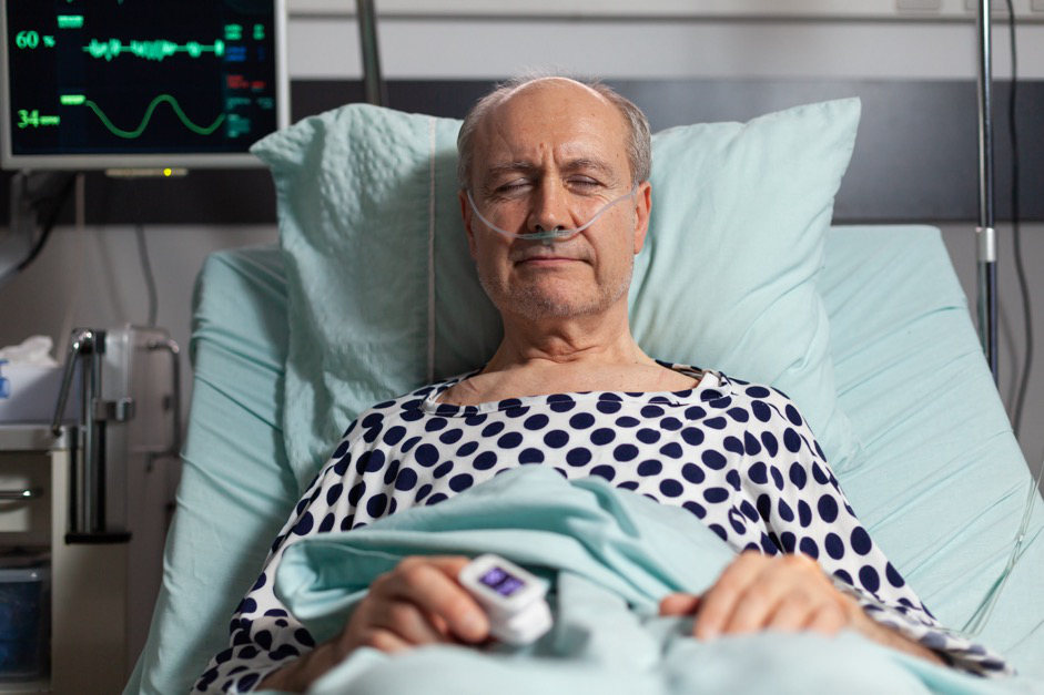 A man looking relaxed during recovery, resting in a hospital bed with a heart monitor in the background.