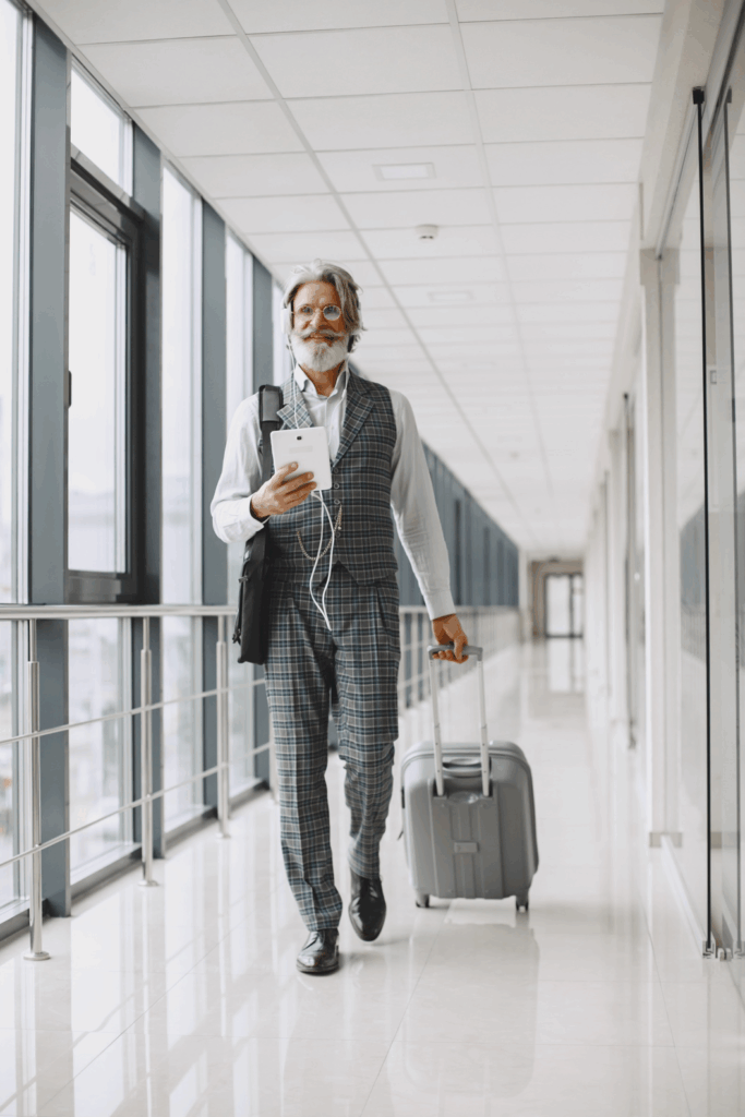 An older man pulling a rolling suitcase, walking confidently through an office.