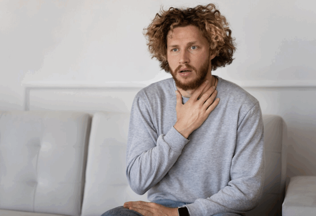 A man experiencing a persistent throat ache, touching his neck in discomfort.